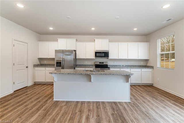 kitchen with light stone counters, appliances with stainless steel finishes, a kitchen island with sink, and white cabinets