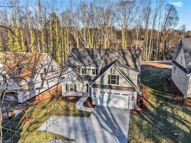 view of front of home featuring a garage, brick siding, driveway, a front lawn, and a wooded view