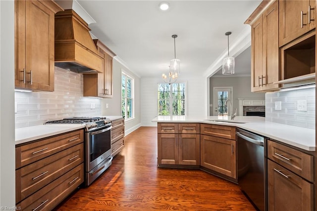 kitchen featuring a peninsula, light countertops, appliances with stainless steel finishes, decorative light fixtures, and custom range hood