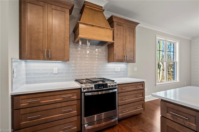 kitchen with brown cabinets, light countertops, decorative backsplash, gas range, and premium range hood