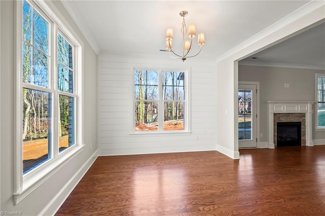 unfurnished dining area featuring dark wood-style flooring, a notable chandelier, a fireplace, ornamental molding, and baseboards