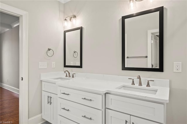 bathroom featuring double vanity, wood finished floors, a sink, and baseboards