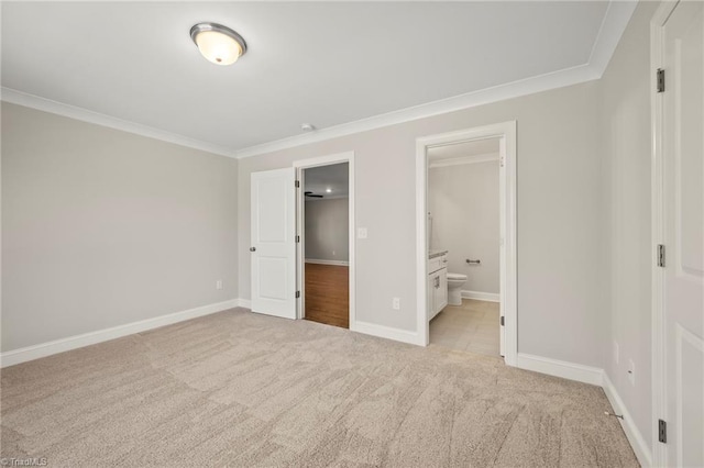 unfurnished bedroom with crown molding, baseboards, ensuite bath, and light colored carpet