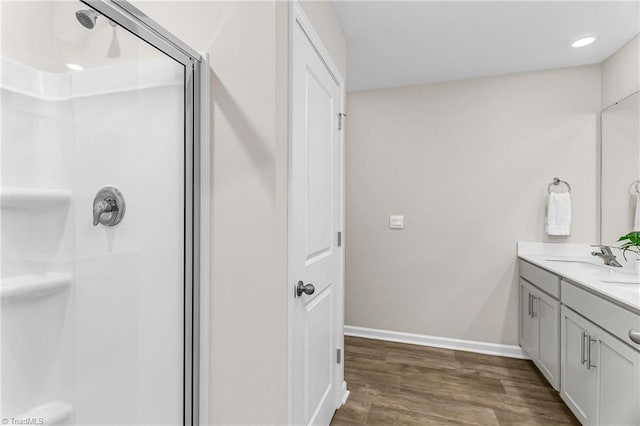 bathroom featuring double vanity, baseboards, wood finished floors, a shower stall, and a sink