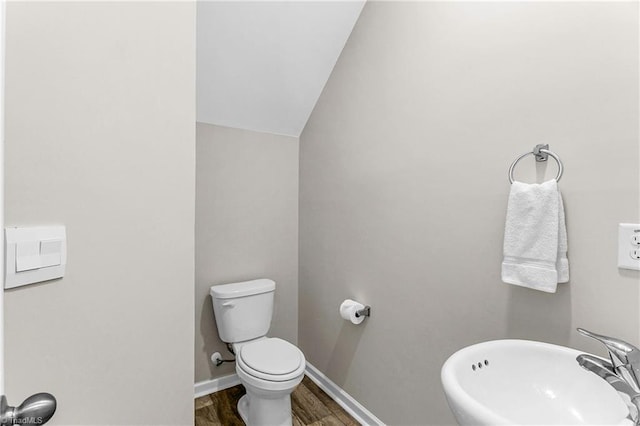 bathroom with toilet, vaulted ceiling, a sink, wood finished floors, and baseboards