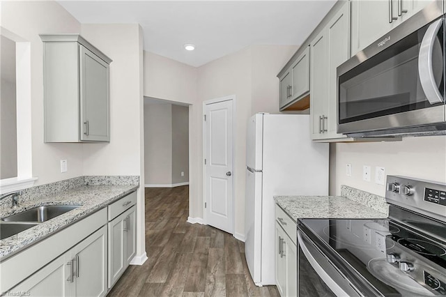 kitchen with stainless steel appliances, a sink, dark wood finished floors, and light stone countertops