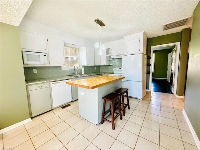 kitchen featuring white appliances, butcher block counters, under cabinet range hood, decorative backsplash, and a textured ceiling
