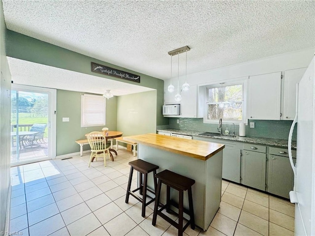kitchen with wood counters, a sink, white appliances, tasteful backsplash, and light tile patterned floors