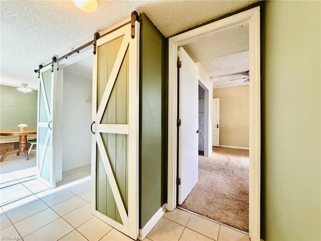 hallway featuring a barn door, a textured ceiling, light tile patterned flooring, and baseboards