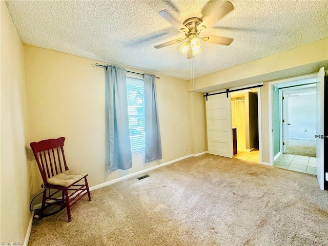 unfurnished bedroom featuring carpet floors, a textured ceiling, a barn door, baseboards, and ceiling fan
