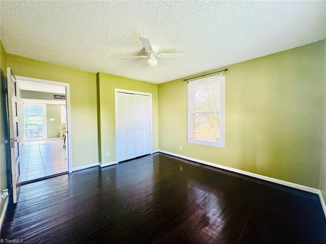 unfurnished bedroom featuring wood finished floors, baseboards, a closet, multiple windows, and a textured ceiling
