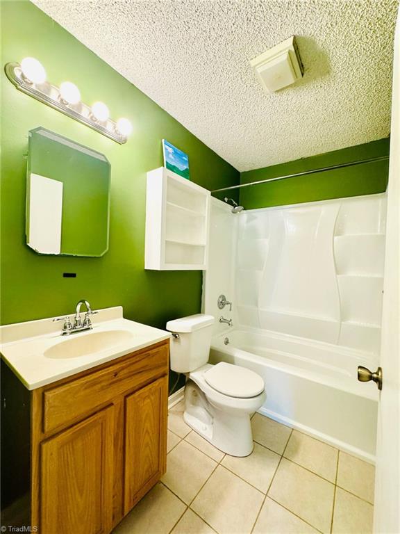 bathroom with a textured ceiling, toilet, vanity, tile patterned floors, and bathing tub / shower combination