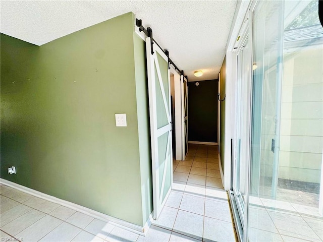 hallway featuring a barn door, a textured ceiling, light tile patterned flooring, and baseboards