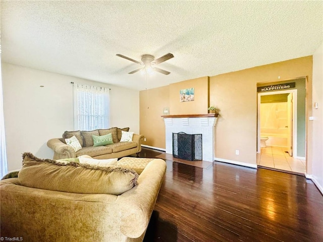 living room featuring wood finished floors, a ceiling fan, a textured ceiling, a brick fireplace, and baseboards
