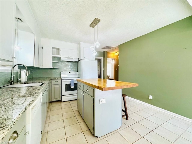 kitchen featuring white appliances, a sink, under cabinet range hood, wood counters, and decorative backsplash