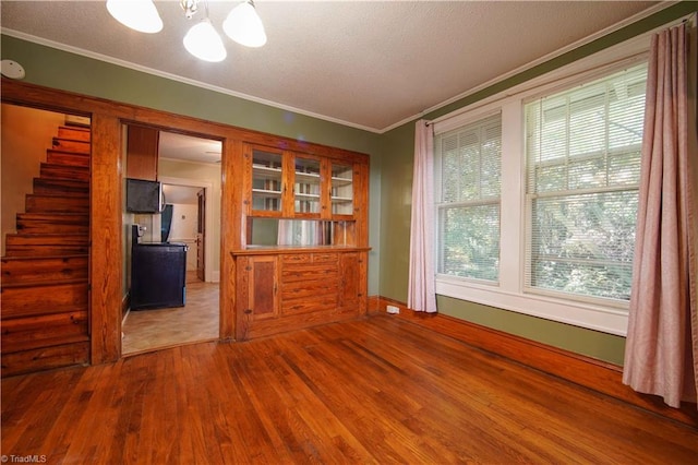 empty room with crown molding, hardwood / wood-style floors, a textured ceiling, and a notable chandelier