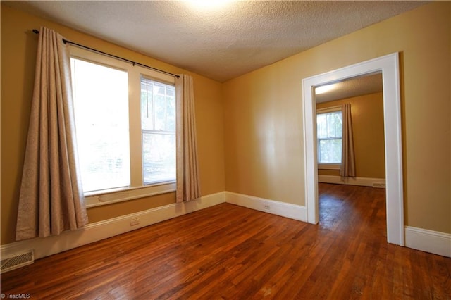 unfurnished room with dark wood-type flooring, a textured ceiling, and plenty of natural light