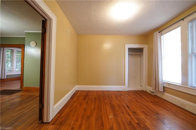 unfurnished bedroom with a closet, dark wood-type flooring, multiple windows, and a textured ceiling