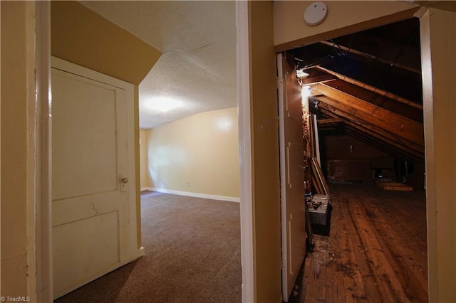 corridor with a textured ceiling, hardwood / wood-style flooring, and vaulted ceiling