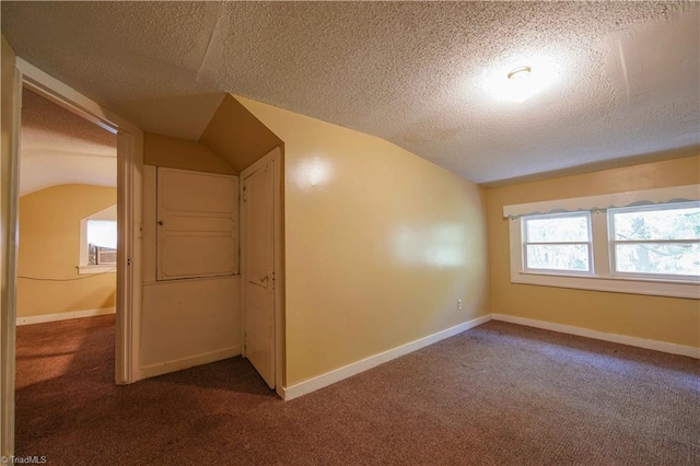 bonus room featuring a textured ceiling, vaulted ceiling, and dark colored carpet