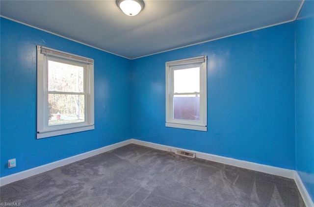 spare room featuring a healthy amount of sunlight, dark carpet, and visible vents