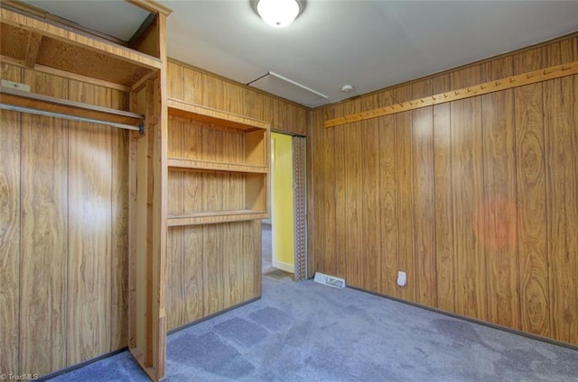 unfurnished bedroom featuring carpet flooring, wooden walls, and visible vents