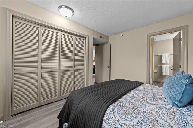 bedroom featuring a closet, light wood-type flooring, a textured ceiling, and connected bathroom