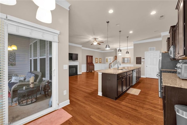 kitchen with an island with sink, crown molding, light stone countertops, dark brown cabinetry, and pendant lighting