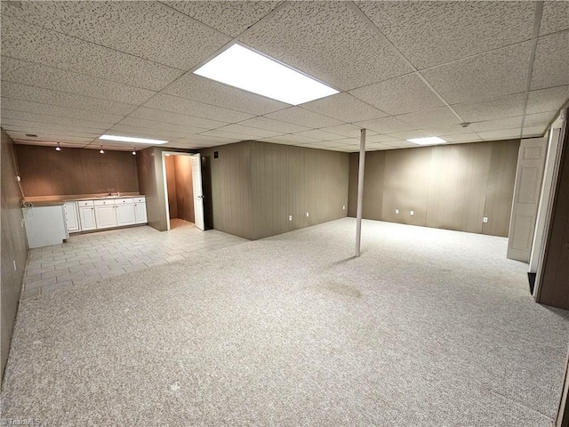 basement with light colored carpet, a drop ceiling, and wooden walls