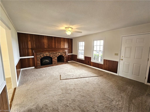 unfurnished living room with wood walls, crown molding, light carpet, a textured ceiling, and a brick fireplace