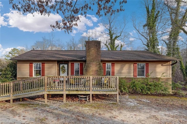 ranch-style home with brick siding, a chimney, and a wooden deck