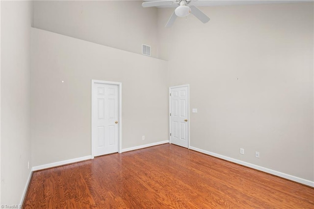 spare room with ceiling fan, a high ceiling, and wood-type flooring