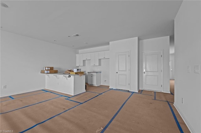 kitchen featuring white cabinetry, kitchen peninsula, a breakfast bar area, and concrete floors