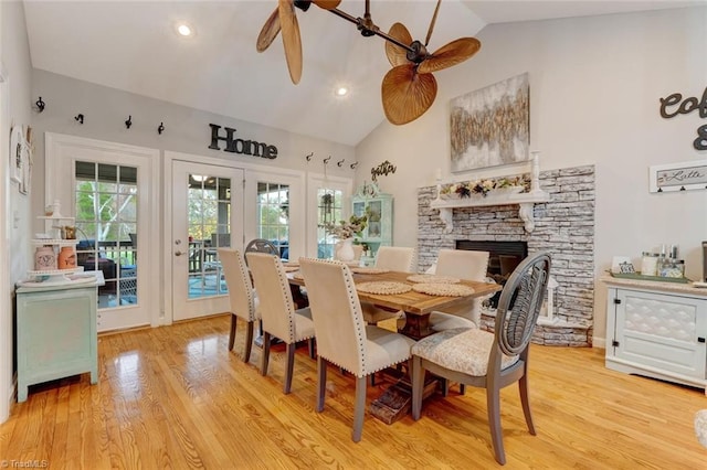 dining room featuring a stone fireplace, high vaulted ceiling, light hardwood / wood-style flooring, and ceiling fan