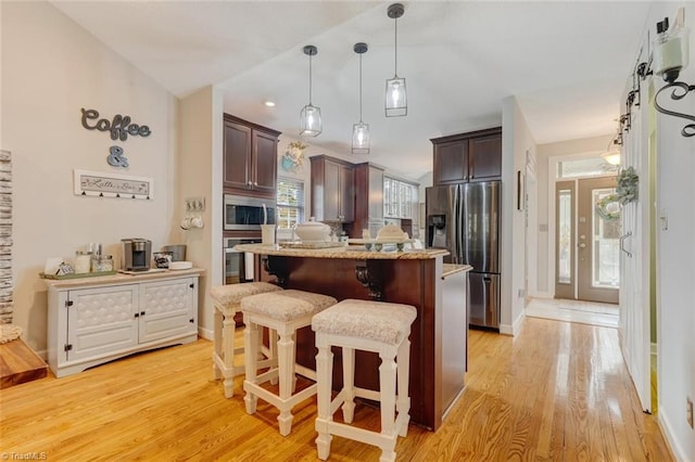 kitchen featuring a center island, a breakfast bar, dark brown cabinets, light wood-type flooring, and appliances with stainless steel finishes