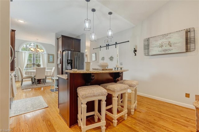 kitchen with light wood-type flooring, a barn door, a notable chandelier, stainless steel refrigerator with ice dispenser, and a kitchen breakfast bar