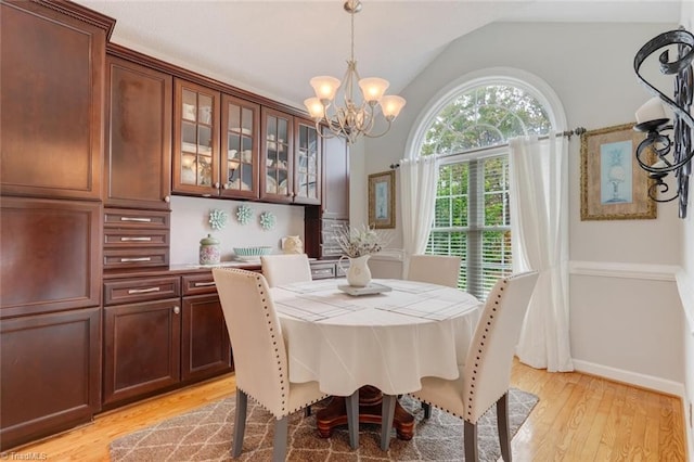 dining room with light hardwood / wood-style floors, a notable chandelier, and vaulted ceiling