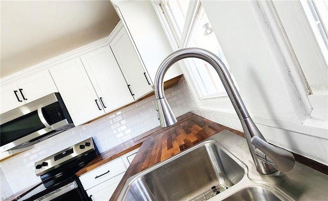 interior space with decorative backsplash, butcher block counters, appliances with stainless steel finishes, white cabinetry, and a sink