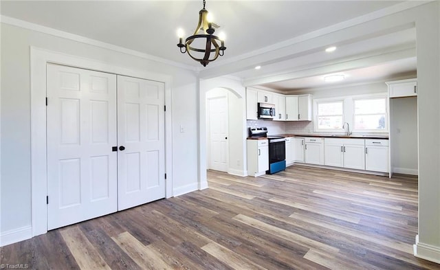 kitchen featuring dark countertops, appliances with stainless steel finishes, ornamental molding, wood finished floors, and white cabinetry