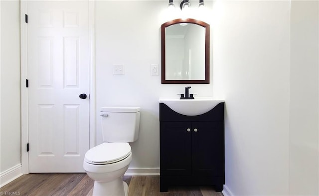 half bathroom with toilet, wood finished floors, vanity, and baseboards