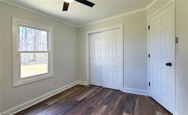 unfurnished bedroom featuring dark wood-type flooring, a ceiling fan, baseboards, a closet, and crown molding