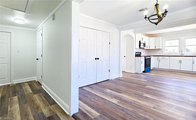 kitchen with arched walkways, crown molding, stainless steel microwave, visible vents, and range with electric cooktop