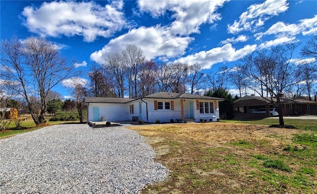 ranch-style home featuring brick siding, a front lawn, and gravel driveway