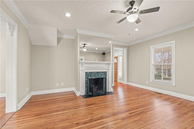 unfurnished living room with ceiling fan, crown molding, light wood-type flooring, and a high end fireplace