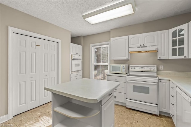 kitchen featuring white cabinetry, light tile floors, a center island, a textured ceiling, and white appliances