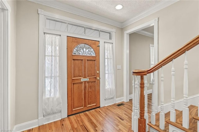 foyer entrance with light hardwood / wood-style flooring, ornamental molding, and a textured ceiling