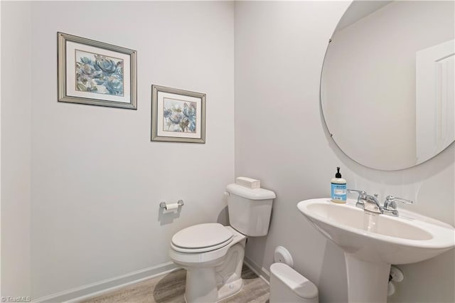 half bathroom featuring wood finished floors, a sink, toilet, and baseboards