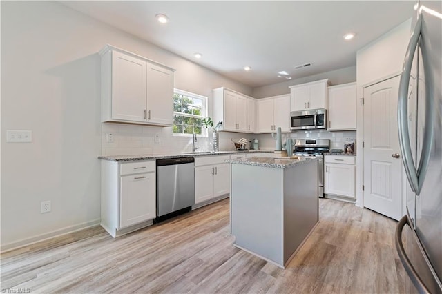 kitchen with stainless steel appliances, white cabinets, and light wood-style flooring