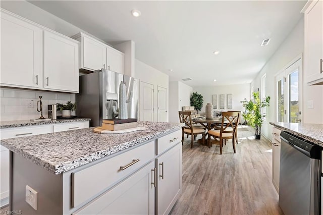 kitchen with stainless steel appliances, visible vents, white cabinets, light wood finished floors, and tasteful backsplash