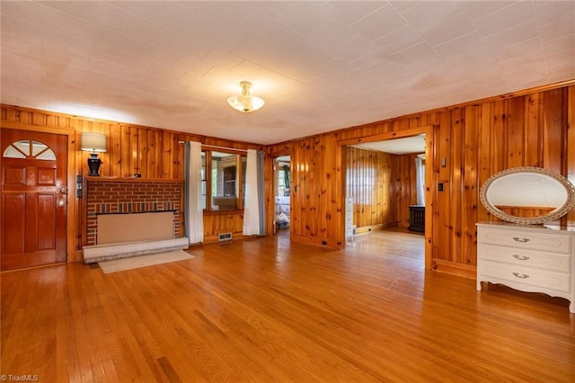 unfurnished living room with wood walls, light hardwood / wood-style flooring, and a brick fireplace